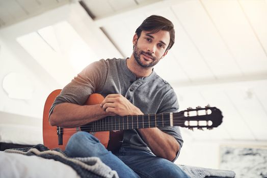 He looks good with a guitar. a handsome young man practising guitar at home.