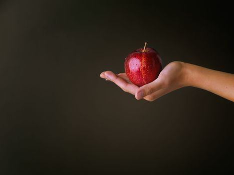 Allure of the scarlet apple. Cropped studio shot of a woman holding a red apple against a dark background.