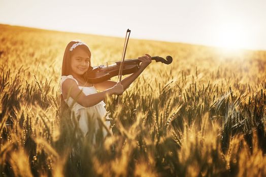 Natures little maestro. Portrait of a cute little girl playing the violin while standing in a cornfield.