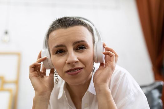 Caucasian adult woman with short haircut listens to music with headphones