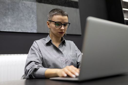 masculine woman programmer with short haircut working on laptop in strong office