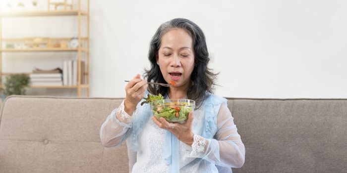 Happy old woman eating healthy vegetable salad at home