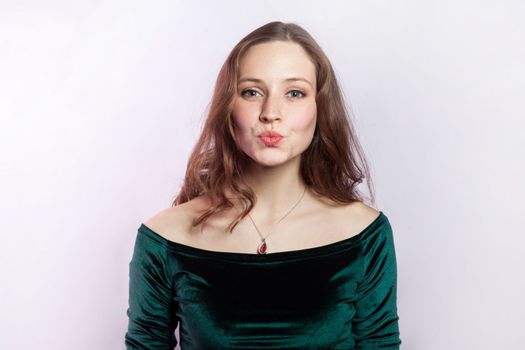 Beautiful gently woman in green dress with pout lips, blowing air kissing, looking at camera.