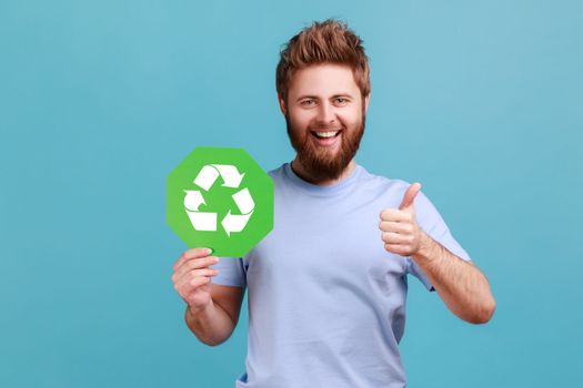 Man showing thumbs up, holding green waste recycling symbol, satisfied with environmental safety.