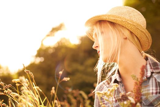 Look deep into nature. Beautiful young woman in a field while wearing a straw fedora.