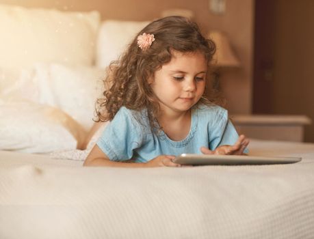 In tune with technology at a young age. an adorable little girl at home lying on her bed playing with a tablet