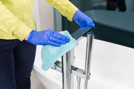 Housekeeper, housewife or hotel maid cleaning freestanding modern chrome tap in bathroom, closeup