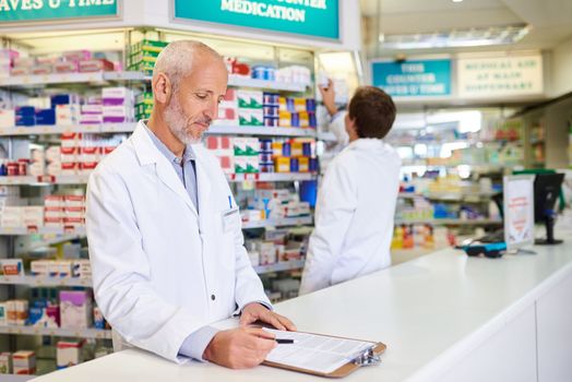 Doing his daily checkup on his pharmaceutical inventory. a mature pharmacist writing on a clipboard in a chemist.