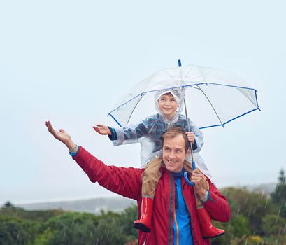The weather wont spoil our fun. a father carrying his son on his shoulders outside in the rain.