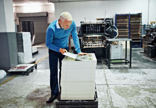 Checking the printing for imperfections. a man checking the quality of a print run in a factory.