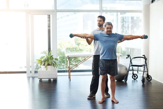 Nice and easy to begin with. a young male physiotherapist helping a mature male patient with movement exercises at a clinic.