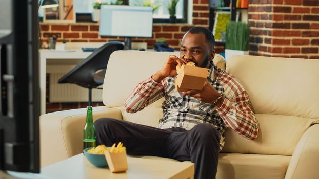 Modern guy eating cheeseburger with fries from takeout