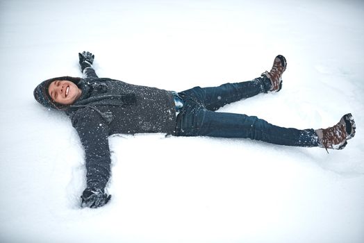 If life gives you snow, make snow angels. a young man lying in the snow making a snow angel.