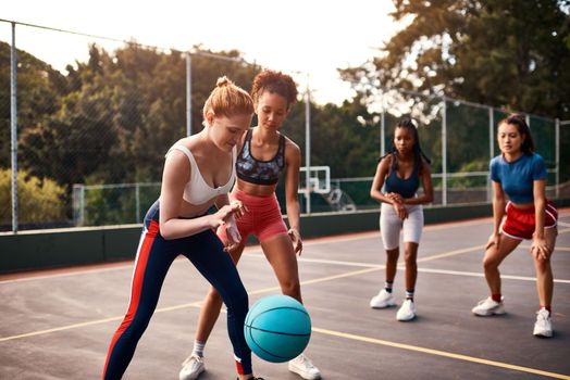 This is a competitive sport. a diverse group of sportswomen playing a competitive game of basketball together during the day.