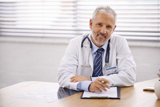 Your health is his top priority. Portrait of a mature male doctor sitting at his desk.