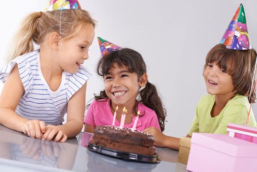 Best friends from a young age. three friends at a birthday party smiling with a cake in front of them.