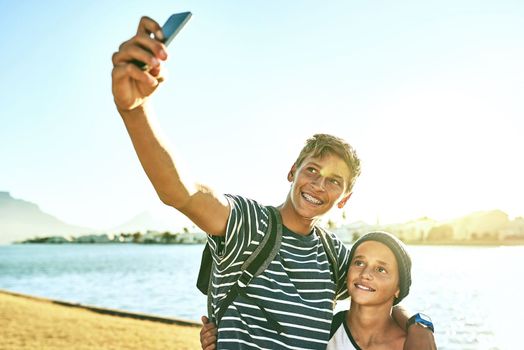 Taking a selfie in the sunshine. two young brothers taking selfies outside with a lagoon in the background.