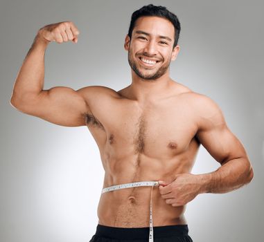 Spend some time at the gym, youll come out stronger. Studio shot of a man flexing his muscles while measuring his waist.