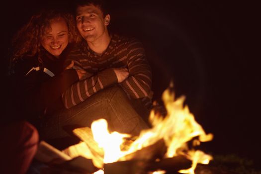 Warm and toasty at the campfire. Smiling young couple sitting outside alongside a fire.