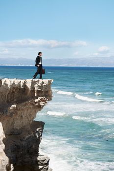 Finding some peace and tranquility. Businessman standing on the edge of a cliff looking out over the ocean.