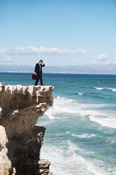 Where to go from here. Confused businessman standing on the edge of a cliff overlooking the ocean.