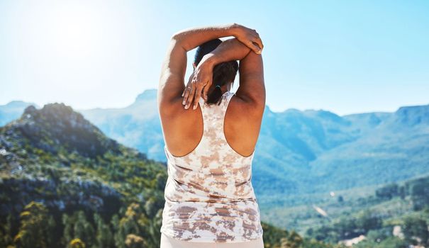 Rear view of a woman stretching her hand behind her head while standing outdoors and overlooking a scenic mountain view