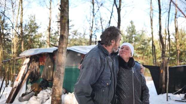 A homeless woman and a man pose in the woods in winter.