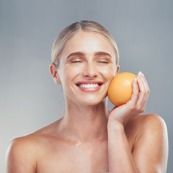 Woman, smile and orange fruit for skincare, beauty and health against grey studio background for cosmetics. Model, skin and face health for self care, vitamin c and cosmetic for organic dermatology