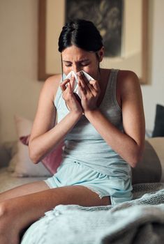 No, not the flu...a young woman blowing her nose with a tissue at home.