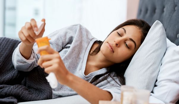 Lets hope this helps. a young woman taking medication while recovering from an illness in bed at home.