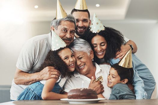 Family, happy birthday and hug portrait of senior woman at a table with a cake, love and care. Smile of children, parents and grandparents together for party to celebrate excited grandma with dessert