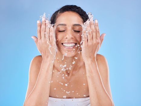 Skincare, water and woman washing face for clean, healthy and natural wellness against a blue studio background. Beauty, cleaning and happy model with splash for facial satisfaction and routine