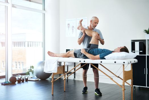 Hes got a gentle approach to rehabilitation. Full length shot of a handsome mature male physiotherapist treating a patient.