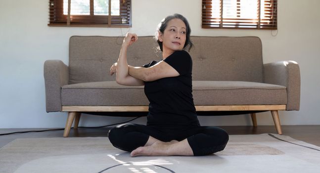 Healthy and elderly woman in workout clothes practicing yoga in her living room.