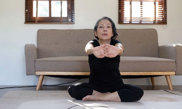 Healthy and elderly woman in workout clothes practicing yoga in her living room.