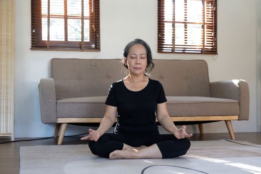 Healthy and elderly woman in workout clothes practicing yoga in her living room