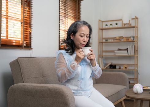 Asian old woman sipping tea in living room at home