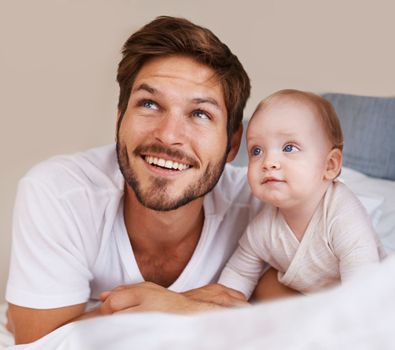 Watch the birdy. a young father and his infant son lying on a bed