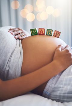 About to be a mom. a pregnant woman with wooden blocks on her belly that spell the word baby.