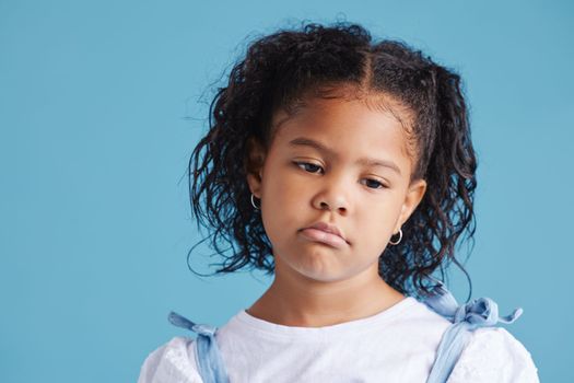 Offended little hispanic girl looking sad and upset while posing against a blue studio background. Unhappy preschooler looking down