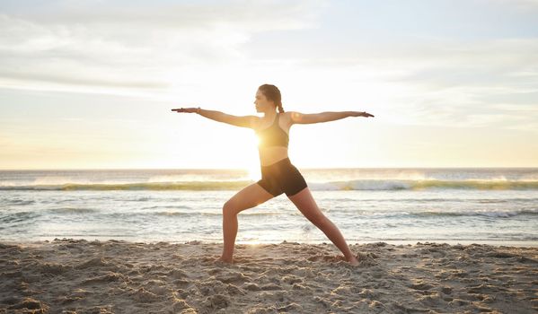 Woman, yoga and meditation on the beach for zen, spiritual wellness or workout in the sunset outdoors. Female yogi meditating in warrior pose for calm, peaceful mind or awareness by the ocean coast