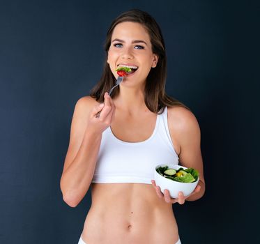 Eating healthy is how I stay in shape. Studio portrait of an attractive young woman eating a salad against a dark background.