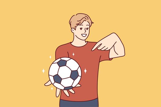 Young man holds soccer ball and points finger at it, offering to play football. Vector image
