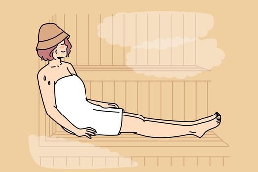 Woman in body towel sits, sweating on bench in sauna.