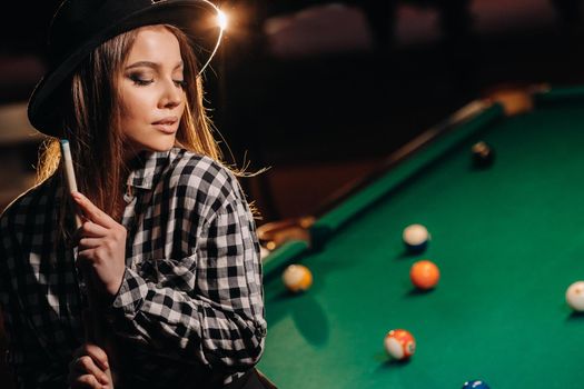 A girl in a hat in a billiard club with a cue in her hands.billiards Game
