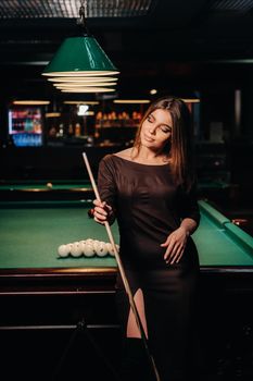 A girl in a hat in a billiard club with a cue in her hands.Pool Game