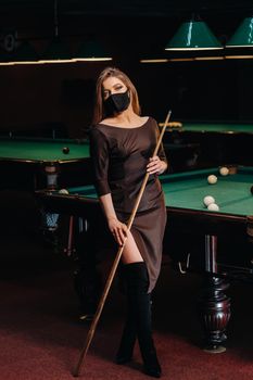 Masked girl in a pool club with a cue in her hands