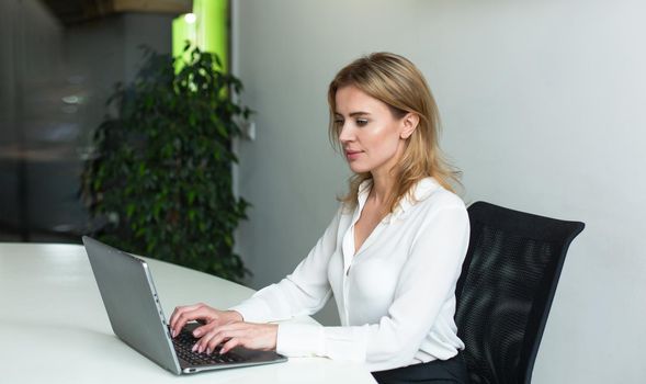 Pretty businesswoman working with computer in office. Young Caucasian lady typing at laptop