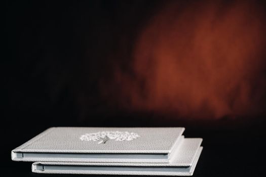 Composition of photo books in natural white leather of different sizes. The white paper on a dark background