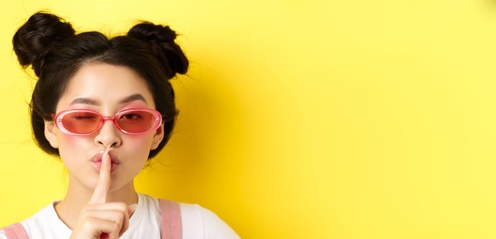 Summer fashion concept. Close-up portrait of glamour asian woman in sunglasses telling a secret, asking be quiet, making hush taboo sign and winking at camera